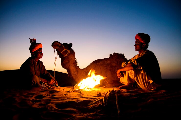 Camel handlers resting by a fire on the dunes at dusk